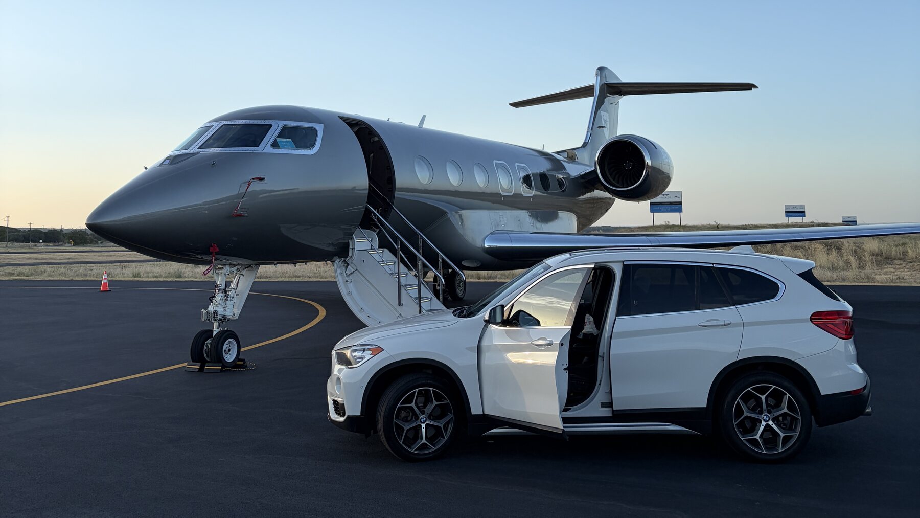 White BMW X1 parked beside a private jet on the tarmac at sunset